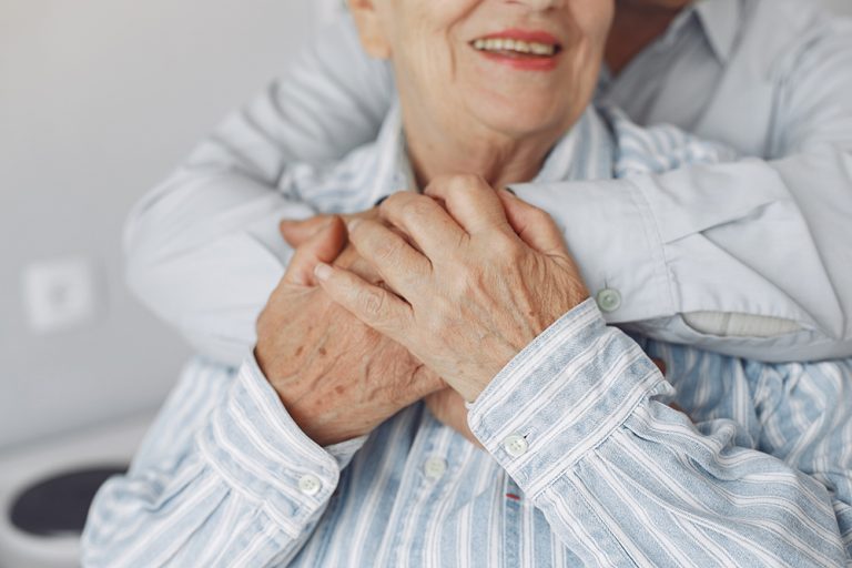 An elderly couple holding each other.