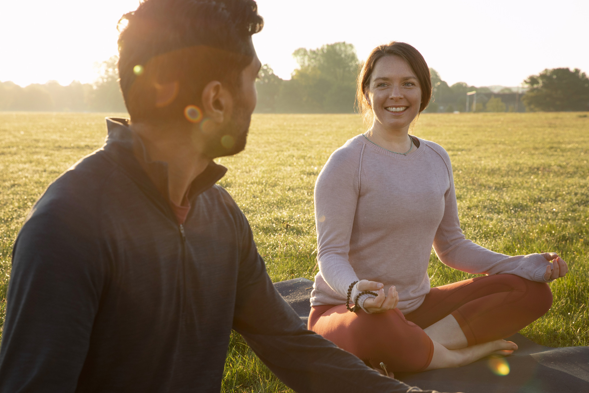 Two people sitting cross legged, practicing yoga outdoors