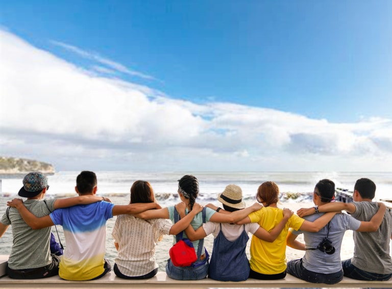 Group of people sat on a wall looking out to sea with their arms linked round eachother
