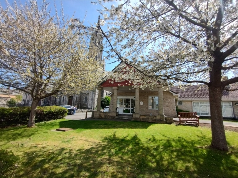 Photo of the Focus Centre building in the spring, photograph shows lovely green grass in the sunshine and cherry trees in blossom in front of the building.