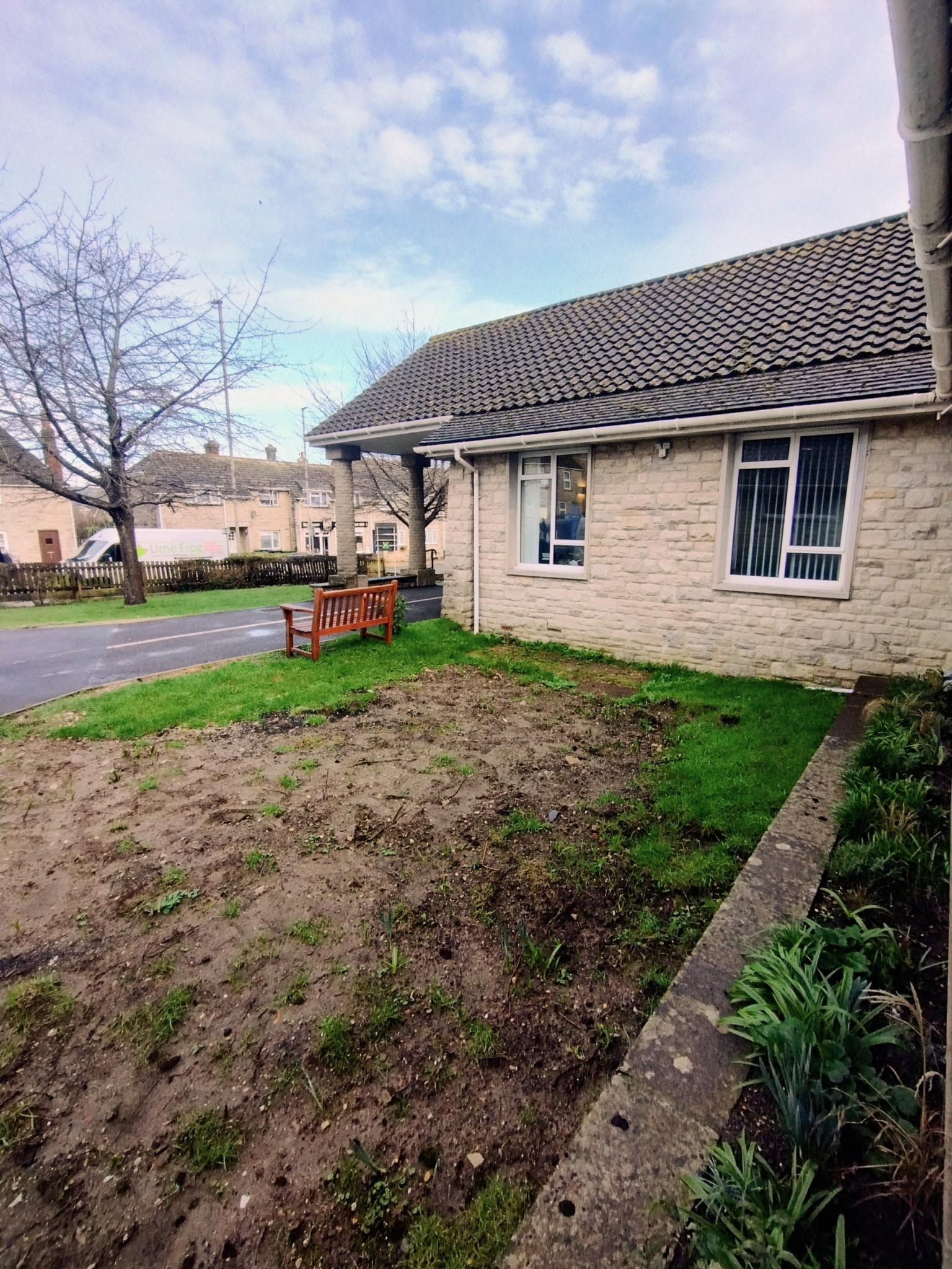 Photograph of the front garden, muddy soil alongside the buildings, showing work that needs to be done to make the gradens a nicer public space.