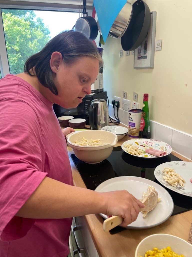 Person in a pink tshirt serving up plates of food, pasta, ham and sweetcorn can be seen.
